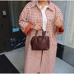 Person wearing a red and white checkered coat holding a brown handbag.
