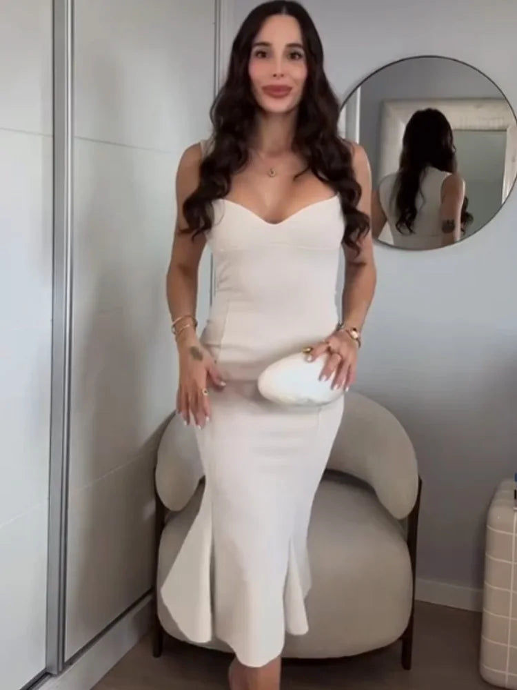 Woman in a white dress standing in front of a mirror in a room.