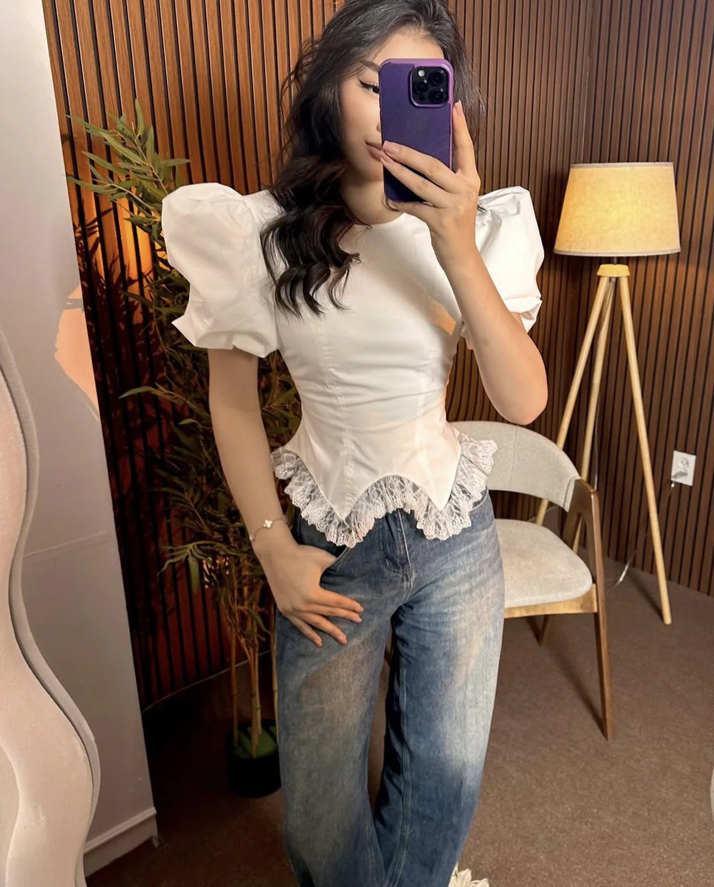 Person wearing a white blouse with puffed sleeves and lace details, paired with blue jeans, taking a mirror selfie.