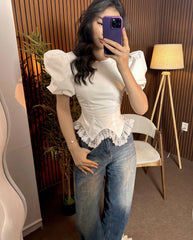 Person wearing a white blouse with puffed sleeves and lace details, paired with blue jeans, taking a mirror selfie.