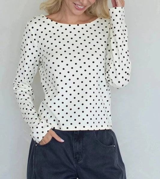 Woman wearing a white long-sleeve top with black polka dots against a light gray background