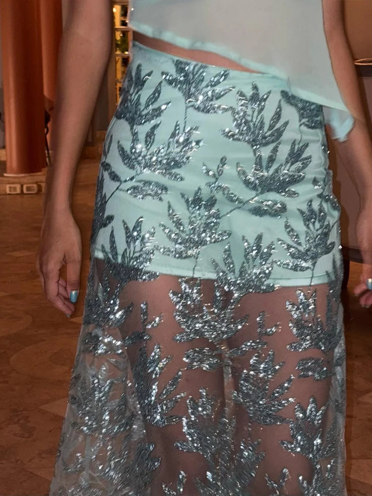 Person wearing a light green skirt with silver sequin leaf patterns on a wooden floor.