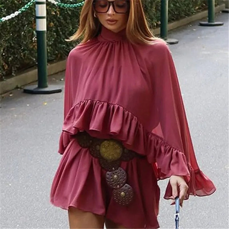 Woman wearing a pink dress with ruffled layers and a belt in an outdoor setting.