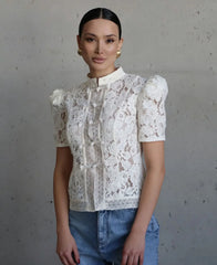 Woman wearing a white lace blouse and blue jeans against a gray background