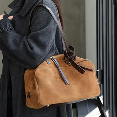 Person holding a brown leather duffel bag with a dark coat.