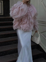 Woman in a pink ruffled top and white satin skirt standing on a staircase.