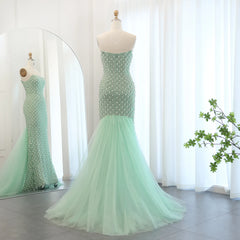 Mannequin displaying glamorous sage green mermaid evening gown with a flowing cape, adorned with pearls and crystals. Golden Ateliers 3