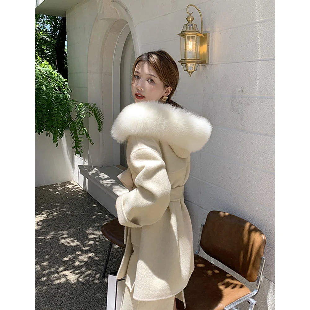 Woman wearing a white coat with a fur hood in an outdoor setting.