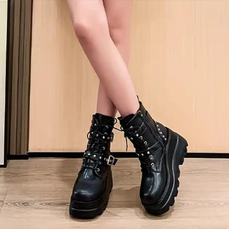 Black leather boots with studded details worn by a person on a wooden floor.