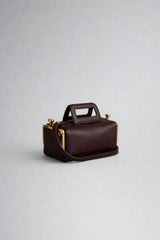 Brown leather handbag with gold accents on a light gray background