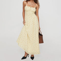 Woman wearing a yellow floral dress holding a brown bag against a white background