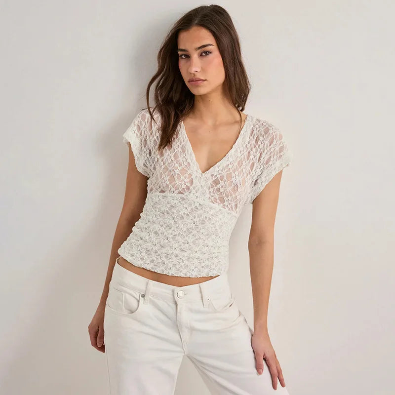 Woman wearing a white lace top and white pants against a plain background