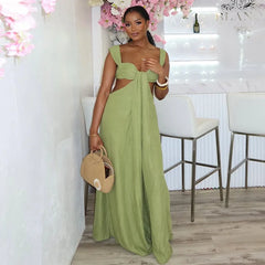 Woman in a green jumpsuit holding a beige handbag in a stylish interior setting.