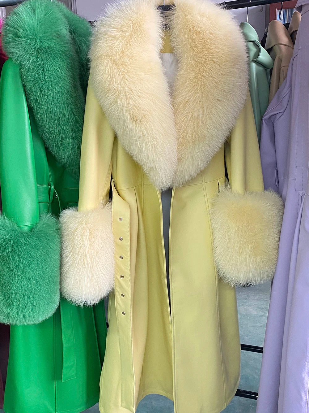 Yellow coat with fur collar and cuffs on a rack with other colorful coats.