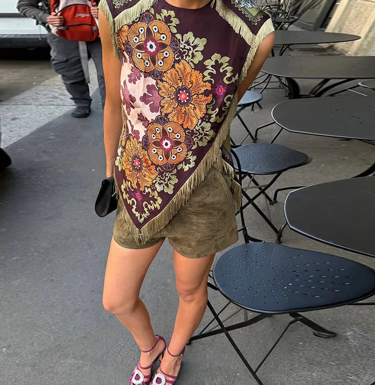 Person wearing a colorful floral shawl over shoulders in an outdoor setting with tables and chairs.