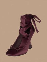 Maroon high-heeled shoe with ribbon detailing on a beige background