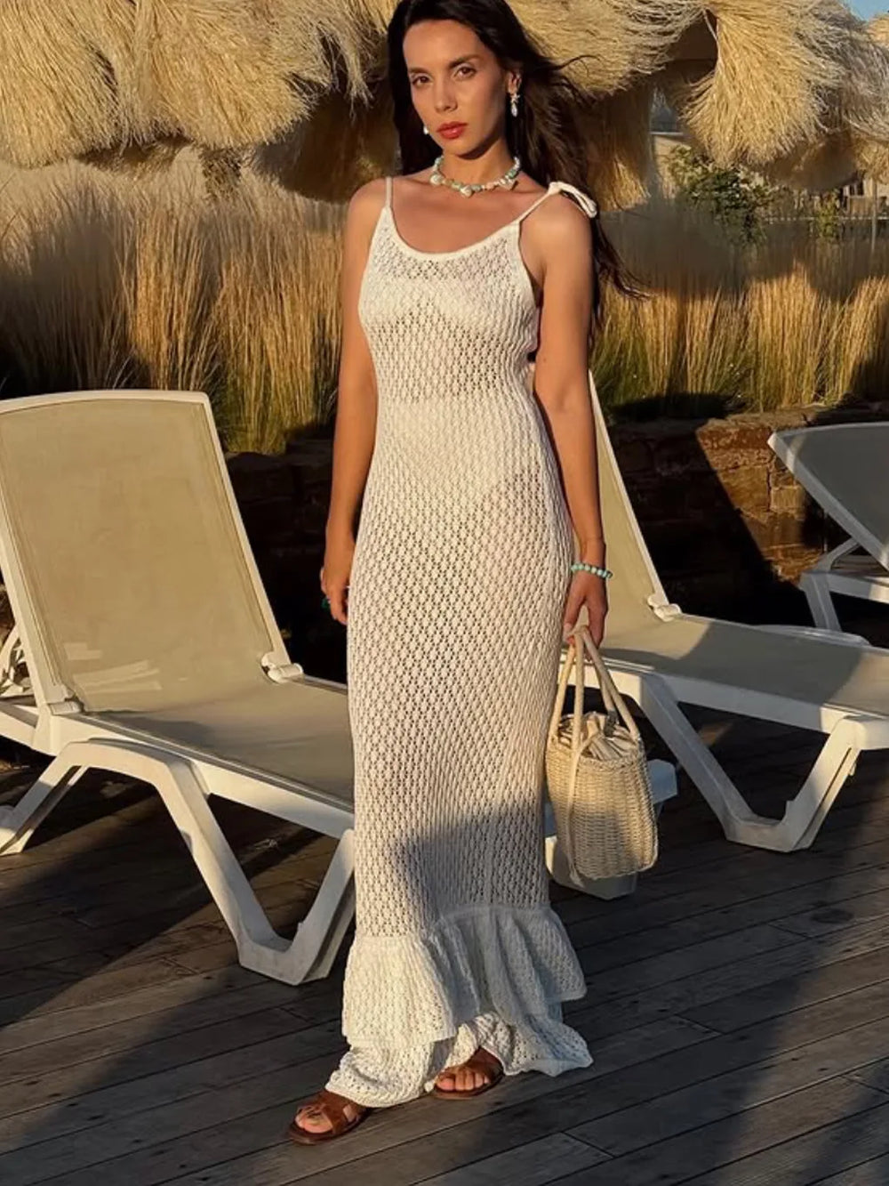 Woman in a white dress standing on a wooden deck with lounge chairs and straw decorations.