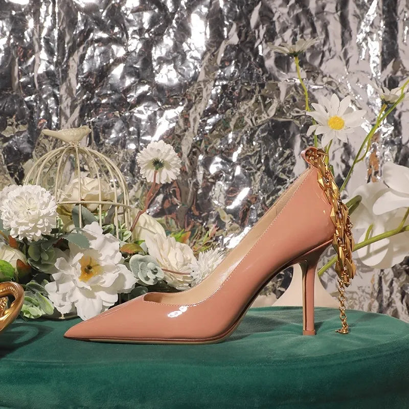 Pink high-heeled shoe with gold chain on a green surface with floral decorations and a reflective silver background.