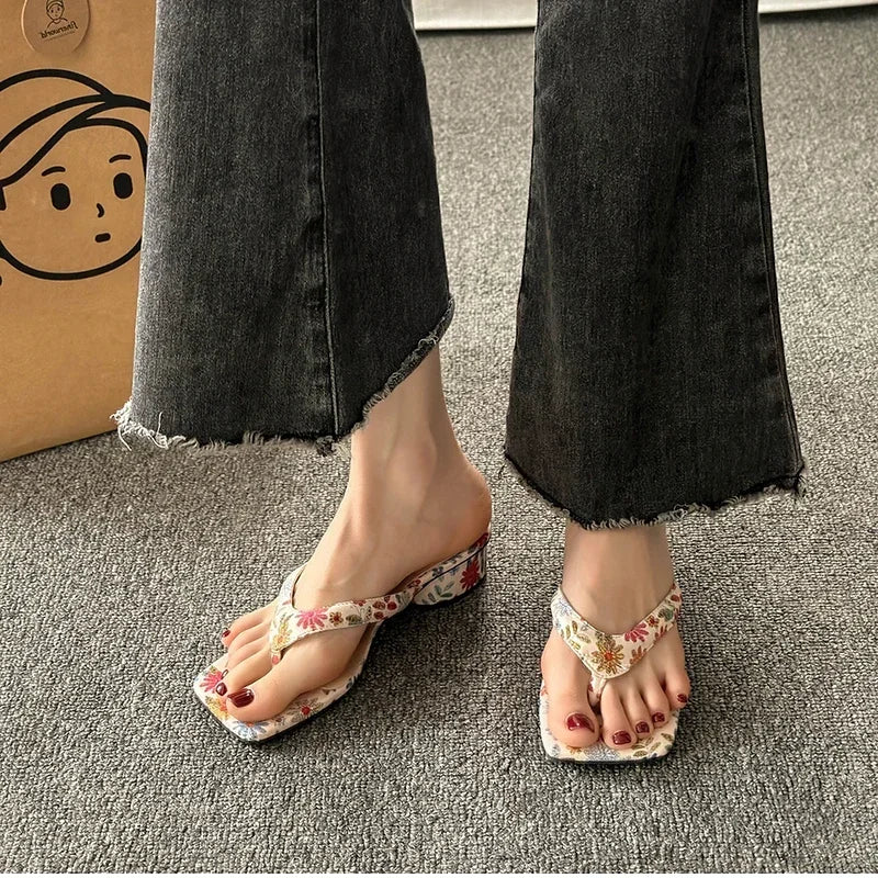 Floral sandals worn with black jeans on a gray floor.