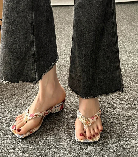 Floral sandals worn with black jeans on a gray floor.