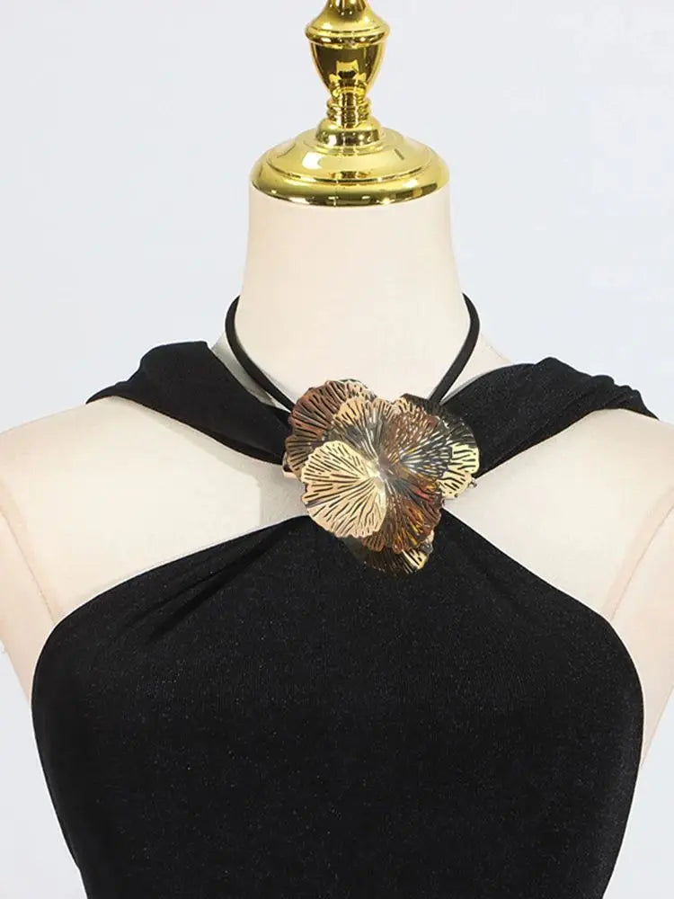 Black halter top with a gold floral accessory on a mannequin against a white background