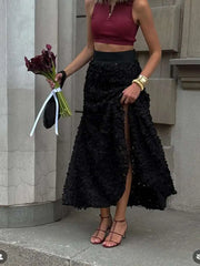 Woman in burgundy top and black lace skirt holding flowers on stone steps.