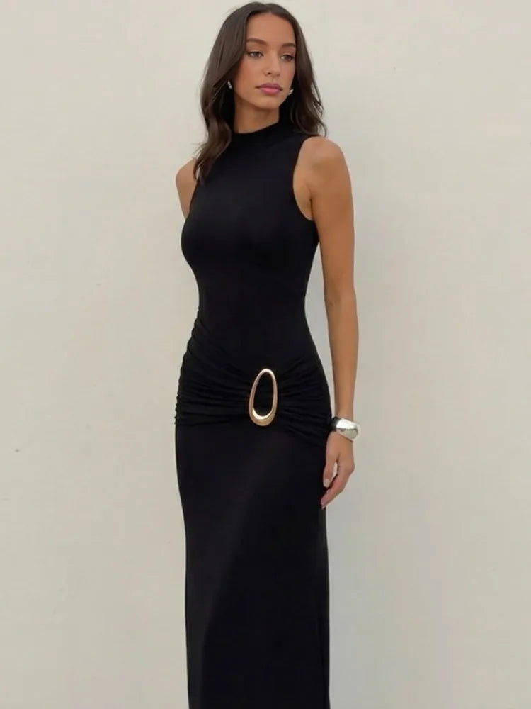 Woman wearing a black sleeveless dress with a gold belt on a plain background