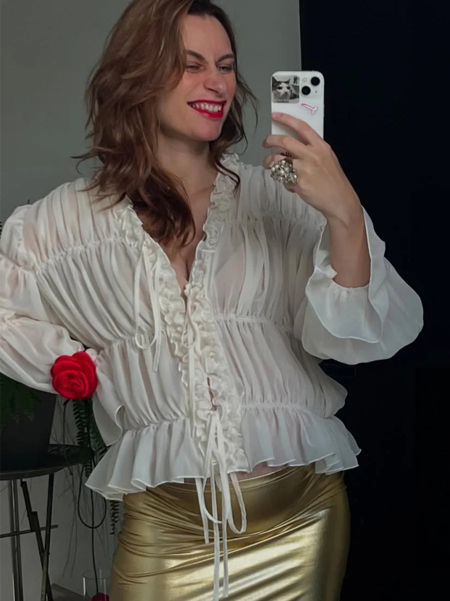 Woman taking a selfie wearing a white blouse and gold skirt, holding a red rose.