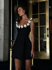 Woman wearing a black dress with white floral details in front of a door.