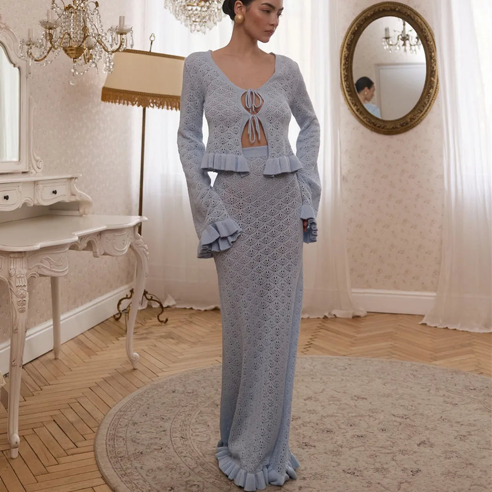 Woman in a light blue knit outfit standing in an elegant room with chandeliers and a mirror.