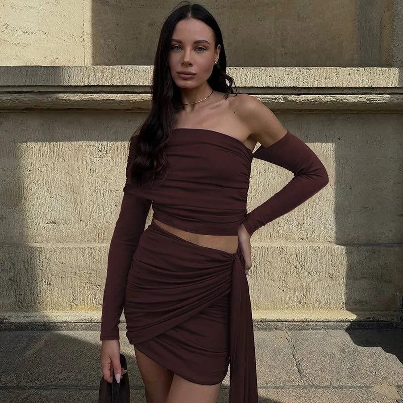 Woman in a brown dress standing against a stone wall.