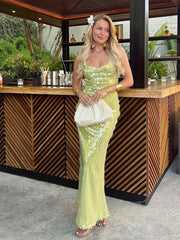 Woman in a green sequin dress holding a white clutch in front of a wooden bar.
