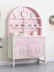 Pink sideboard with decorative plates and teaware against a white wall.
