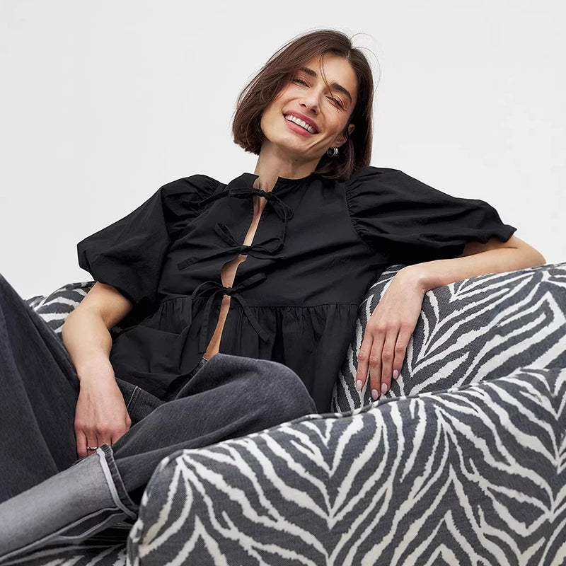 Woman in a black top sitting on a zebra-patterned sofa against a plain background