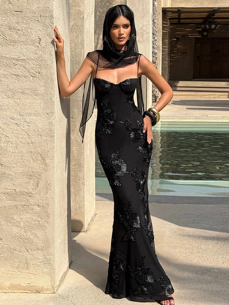 Woman in a black floral dress standing against a stone wall.