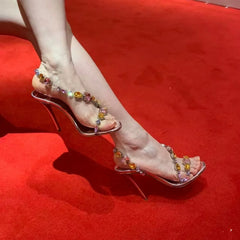 Woman's feet wearing gemstone transparent stiletto heels on a red carpet
