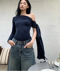 Woman wearing a navy off-shoulder top and jeans, standing indoors with a neutral background.
