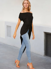 Woman wearing a black off-shoulder top and light blue jeans in an indoor setting.