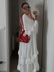Person wearing a white dress holding a red handbag in a neutral setting