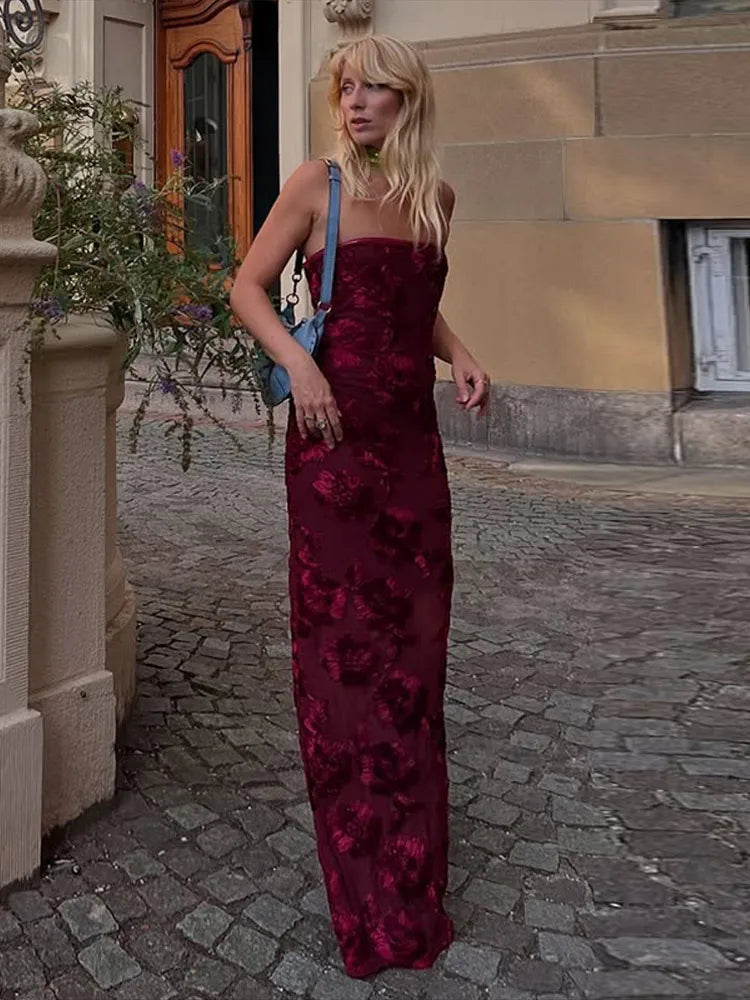 Woman in a burgundy floral dress standing on a cobblestone street.
