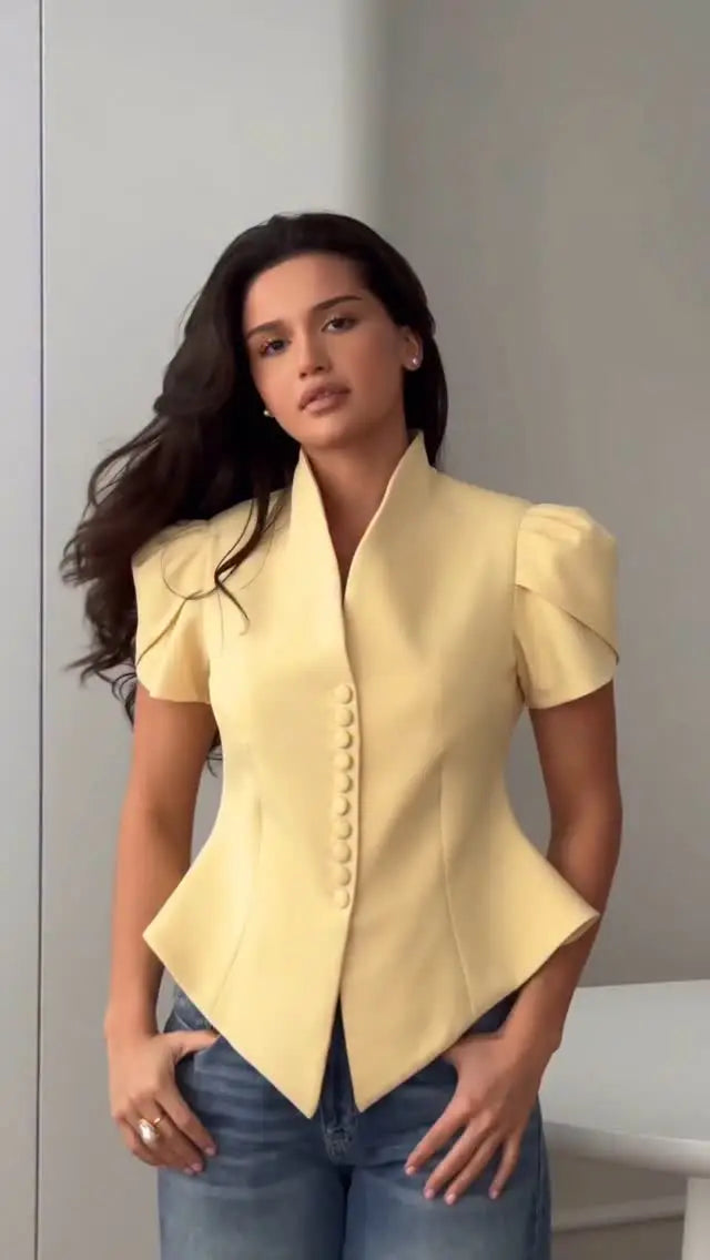 Woman wearing a yellow blazer and blue jeans against a neutral background