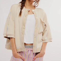 Woman wearing a beige jacket over a white top and striped pants on a plain background