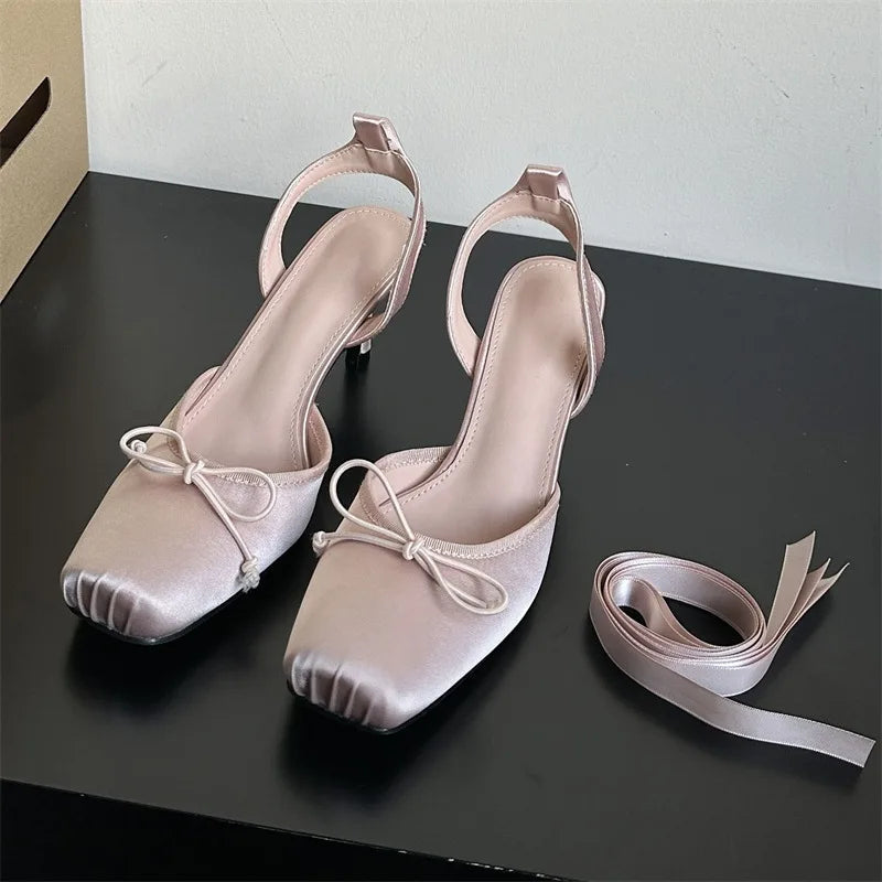 Pair of light pink high-heeled shoes with bow details on a black surface.