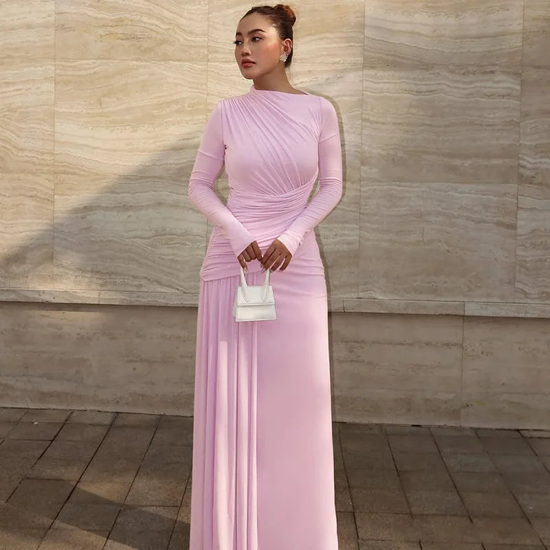 Woman in a pink dress holding a white handbag against a beige wall.