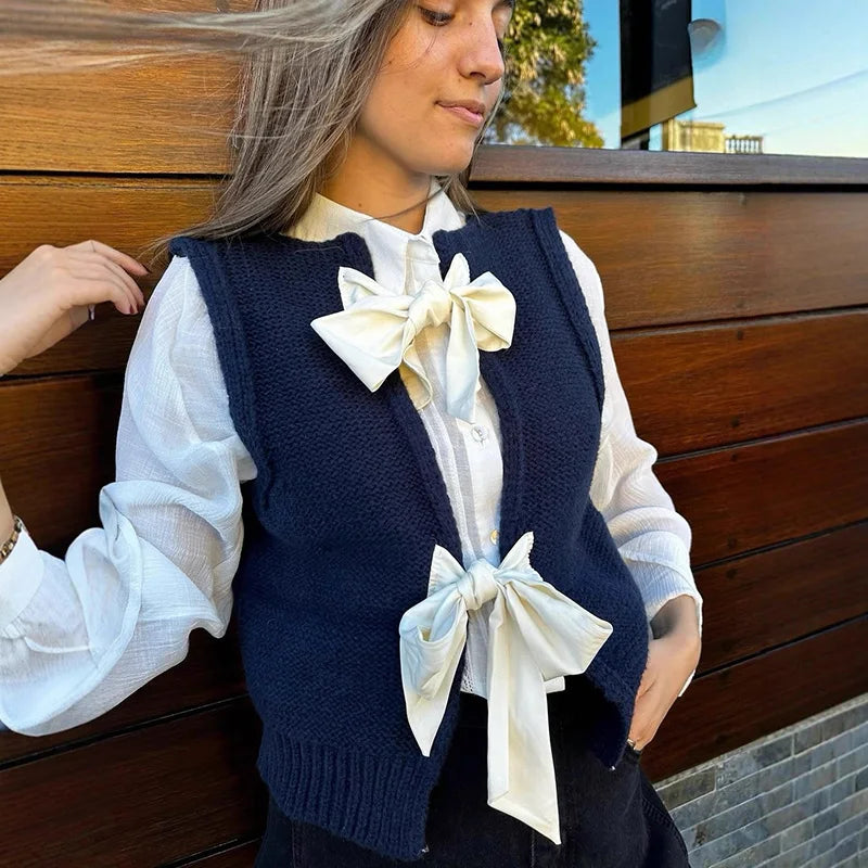 Woman wearing a navy blue vest with white ruffled blouse and decorative bows against a wooden background
