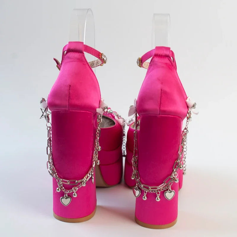 Pair of bright pink high-heeled shoes with chain and heart charm details on a white background