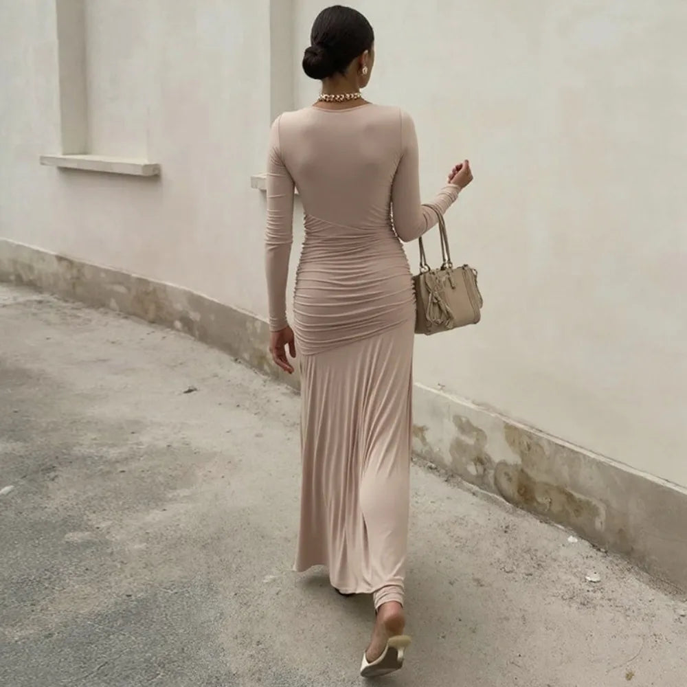 Woman in a long beige dress walking away from the camera against a plain wall.