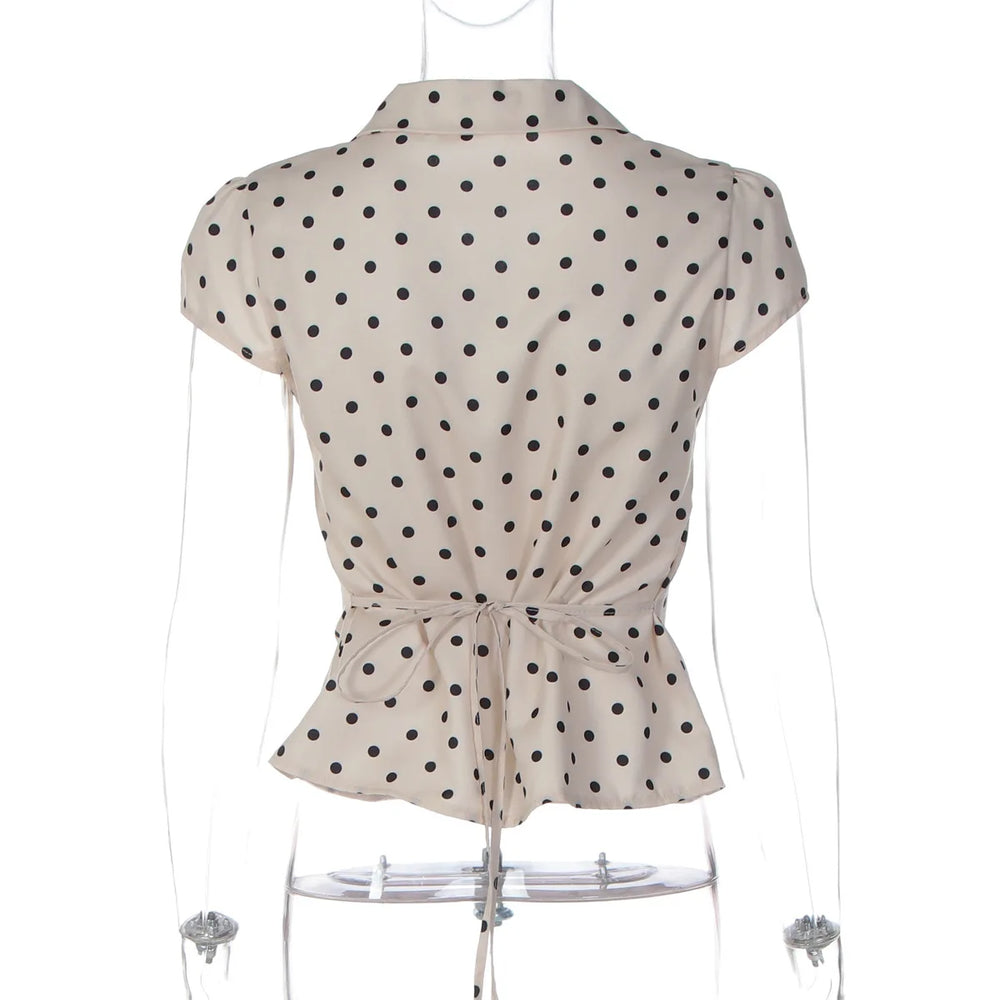 Beige top with black polka dots on a mannequin against a white background