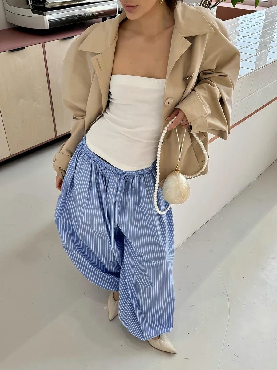 Person wearing a beige jacket, white top, and blue striped pants in an indoor setting.