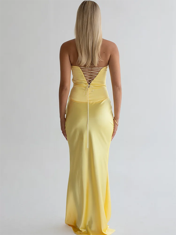 Woman wearing a yellow evening gown with a backless design on a plain background